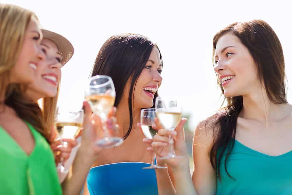 Four women smiling and holding wine glasses outdoors during a bachelorette party in St. Augustine.