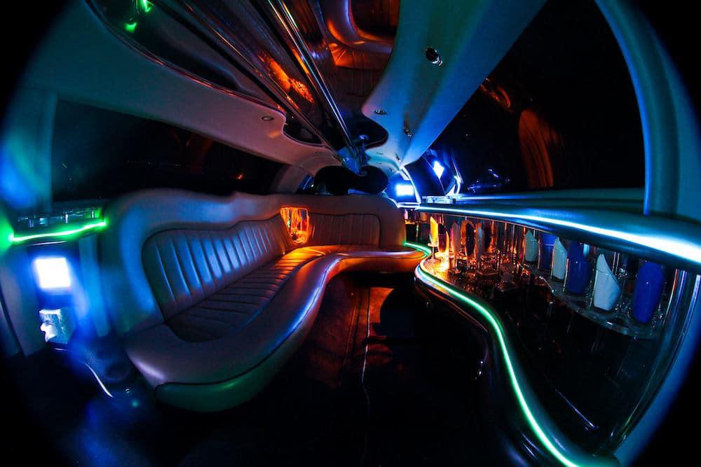 Interior of a limousine with colorful LED lighting, a leather bench seat, and a built-in bar stocked with various bottles. The ambiance is vibrant and luxurious—perfect for exploring the Top 8 Bachelorette Party Ideas in Tallahassee.