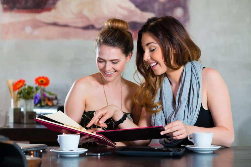 Two women sitting at a table planning Bachelorette Parties in Mansfield/Grand Prairie, while looking at a book.
