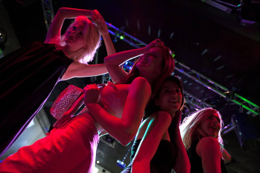 Four people are dancing in a dimly lit environment with colorful lights. They are posing and smiling, enjoying the moment.