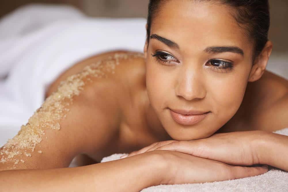 A woman laying on a towel with sand on her back.