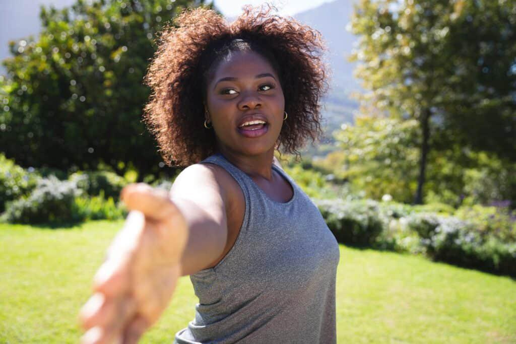 A young black woman with curly hair standing in a grassy area.