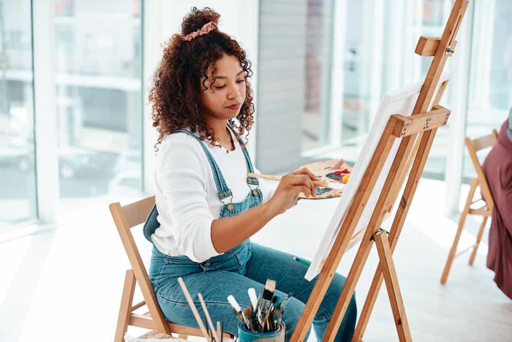 A woman is painting on an easel in an art studio, offering a fun and creative activity for bachelorette parties in Mansfield /Grand Prairie.