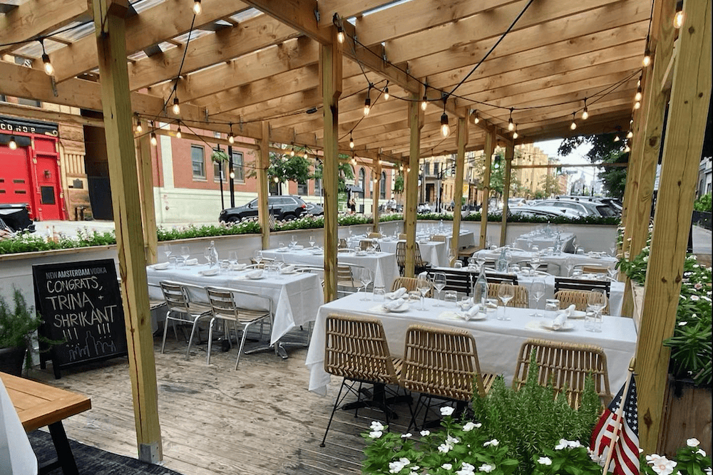 A picturesque outdoor dining area in Hoboken, perfect for bachelorette parties or other special gatherings. Guests can relax and enjoy their meals at comfortable tables and chairs while taking in the beautiful