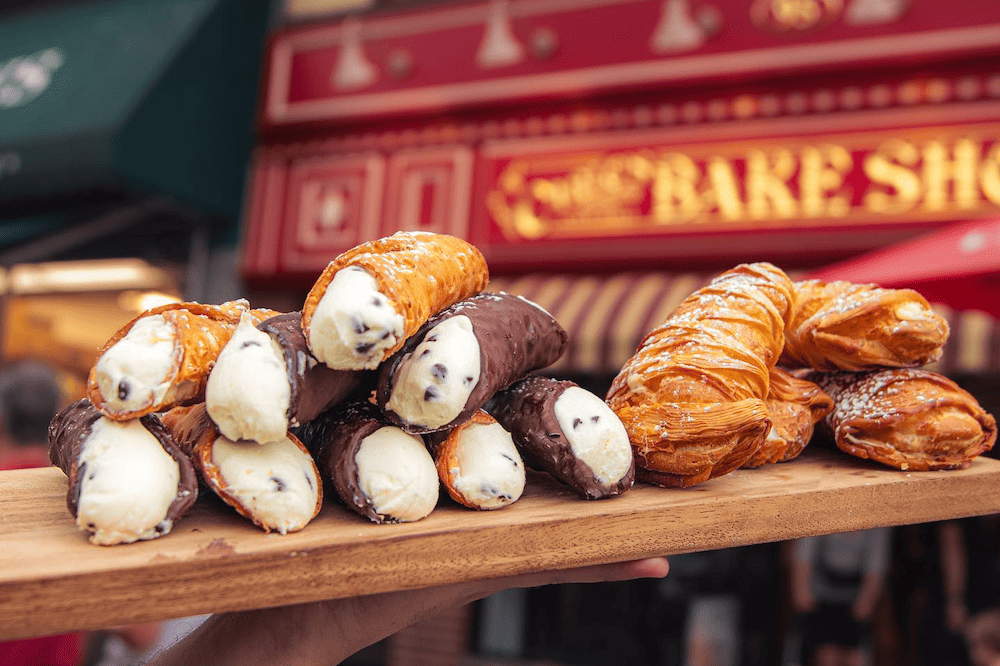 A person is holding a tray of pastries in front of a bakery, offering options for bachelorette parties in Hoboken.