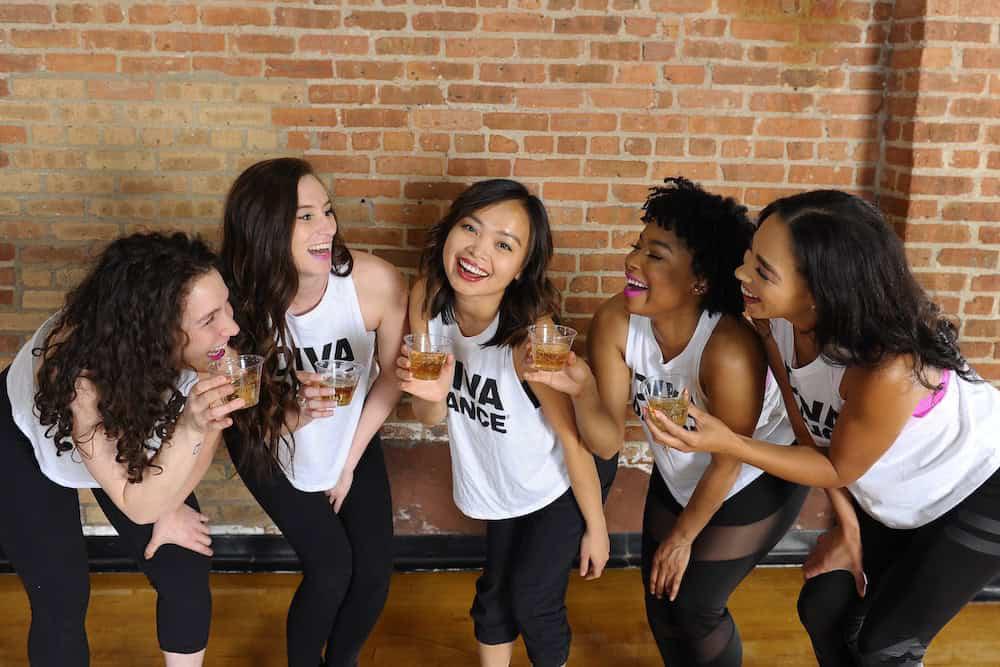 Five women in matching white tanks and black pants, smiling together after class.