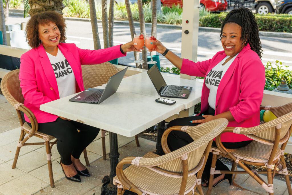 Two women sitting at a table clinking glasses at a divadance bossbabe bootcamp, a great way to get more involved