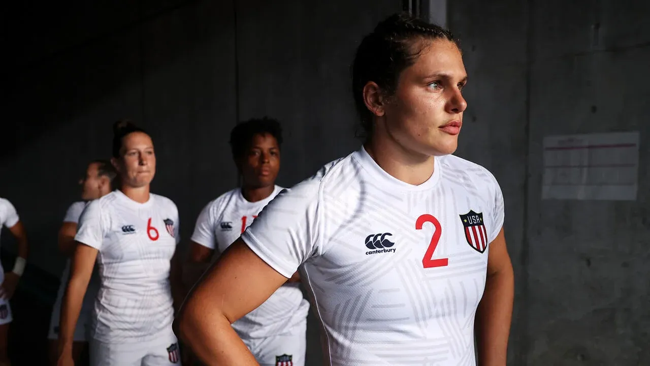 A group of athletes wearing white USA rugby uniforms stands in a line, with one player, number 2, at the front looking focused.