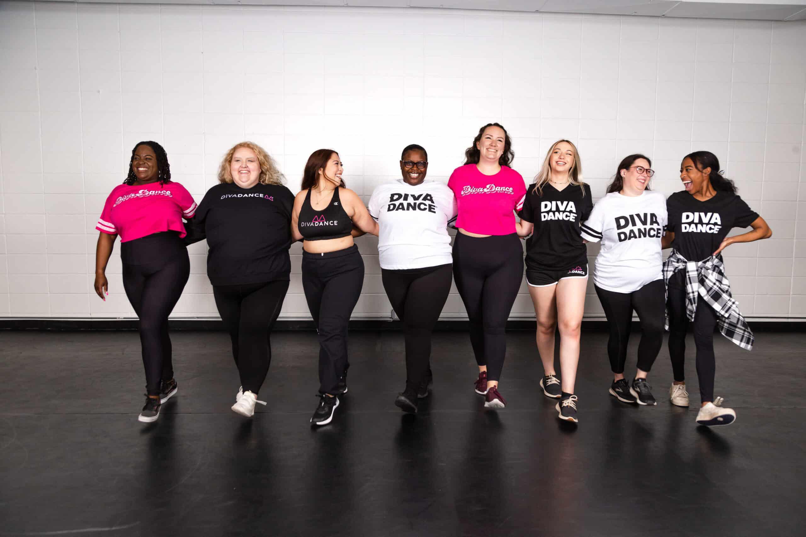 A group of women in black DivaDance t-shirts standing arm-in-arm together.