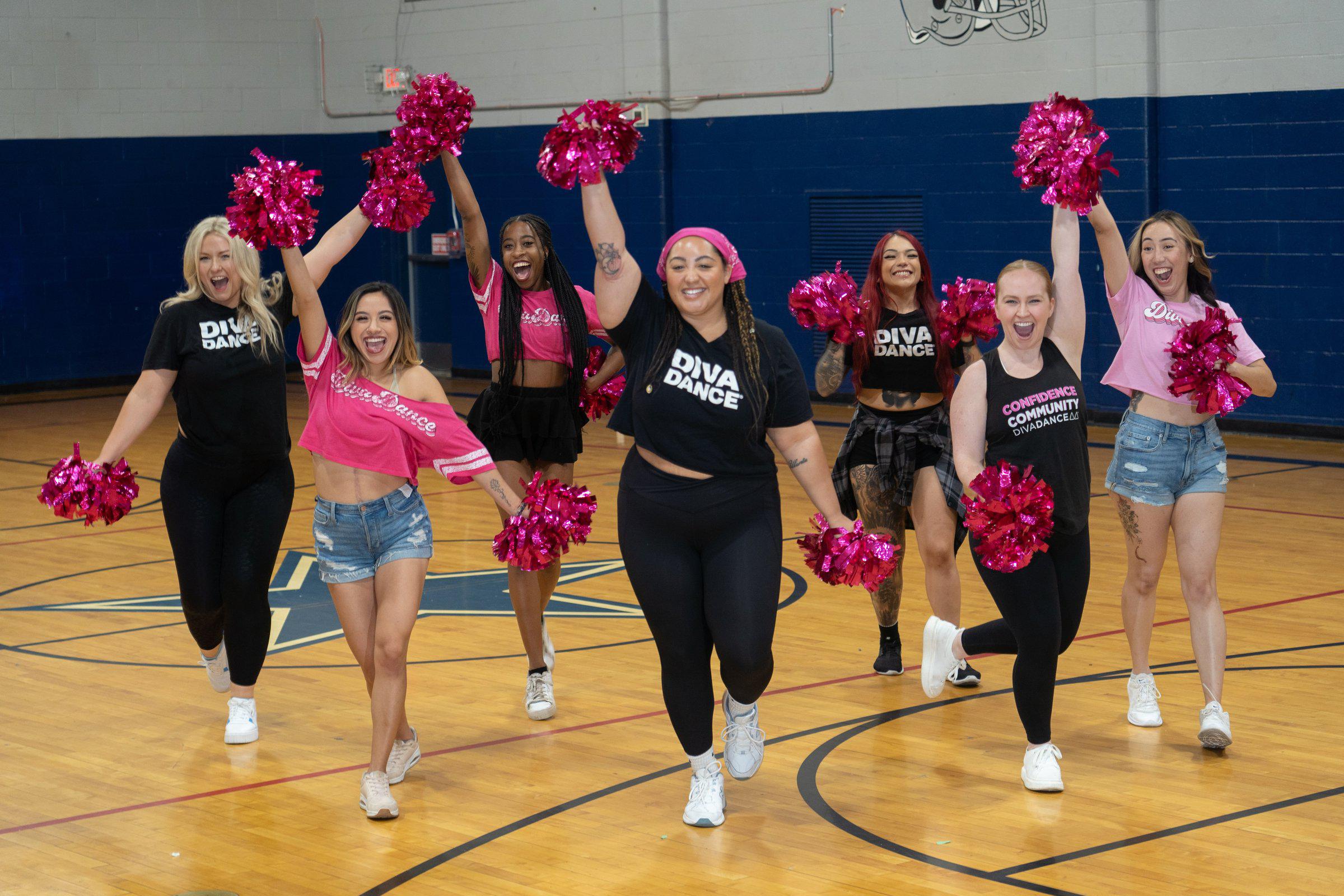 Women in DivaDance shirts cheering with pink pom-poms on a basketball court at a Moms with Poms performance
