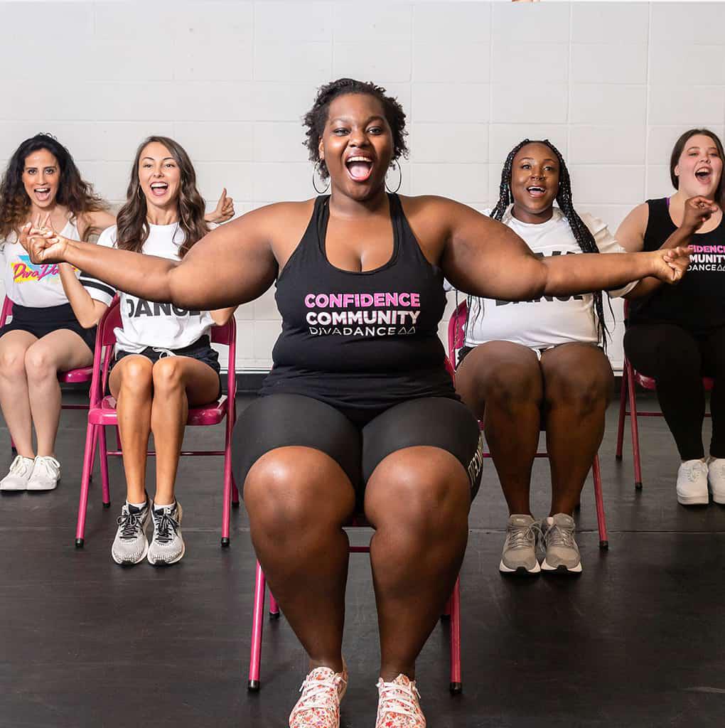 Smiling dancer with hoop earrings and a backpack in front of a pink mural—joyful and confident.