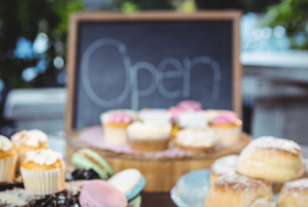 A variety of cupcakes and pastries on a table in front of a chalkboard.