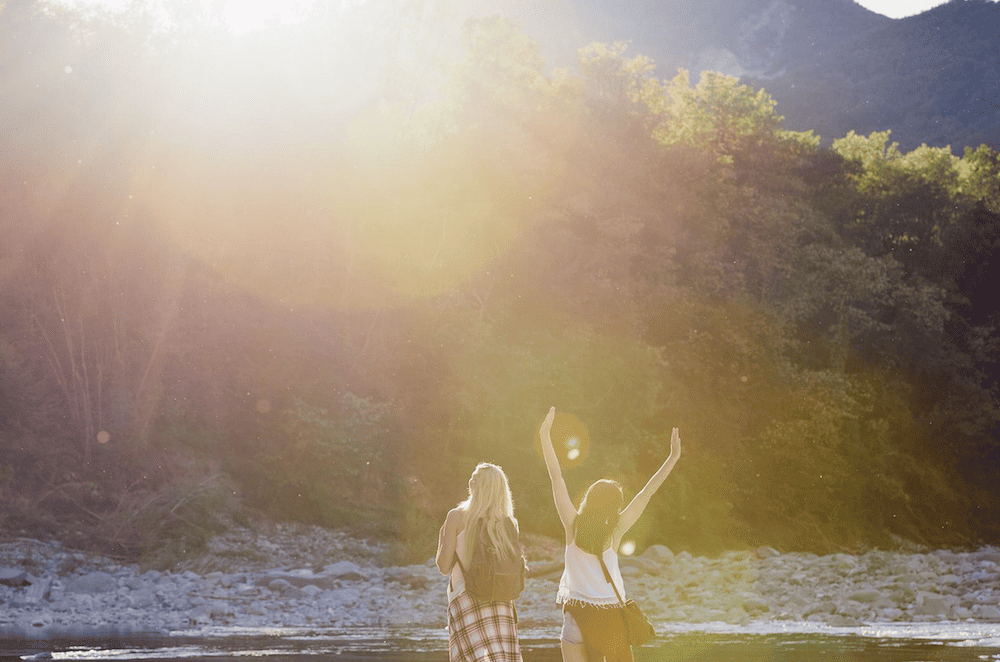 Two women standing in a river with their arms raised.