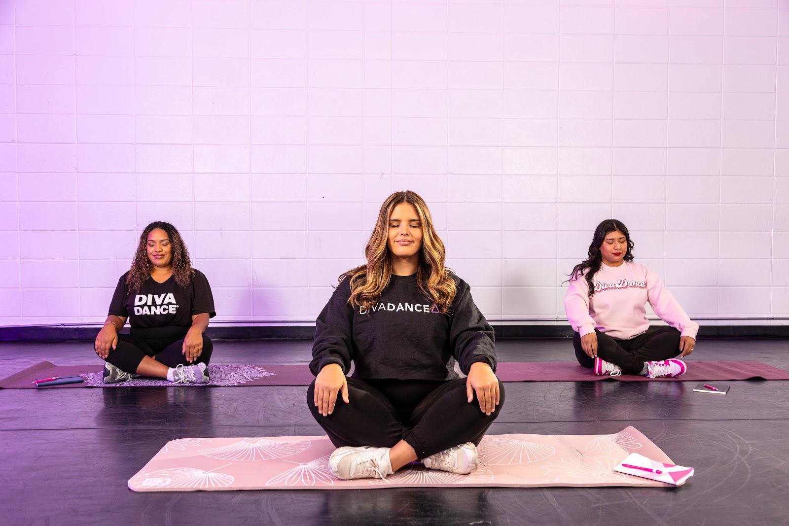 Three women cross-legged in meditation pose with eyes closed during a DanceRx low-impact mindfulness class