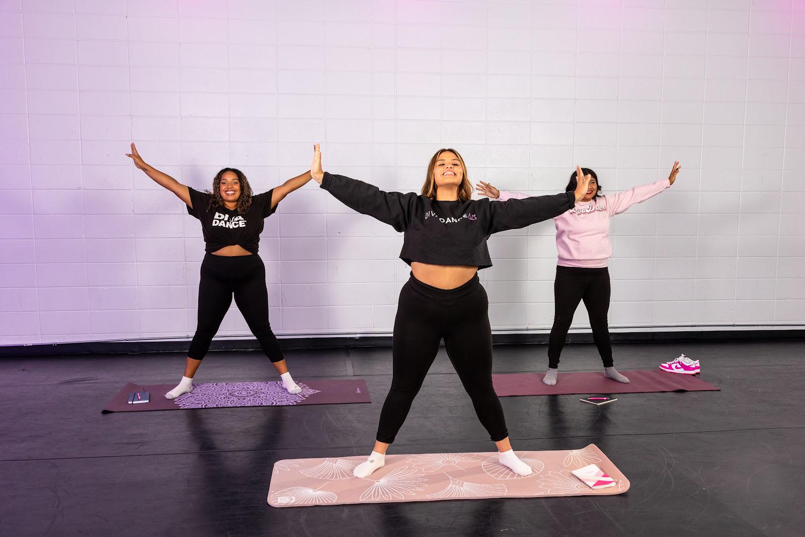 Three women in DivaDance branded apparel celebrating arms-V on yoga mats during a DanceRx wellness class