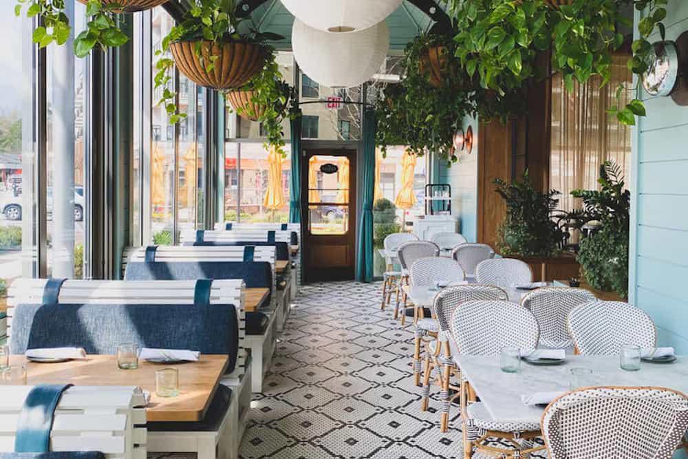 Bright and airy café interior with patterned floor, hanging plants, and wicker chairs.